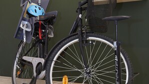 Una silla de ruedas, una bicicleta y un tablero de herramientas contra un muro verde.