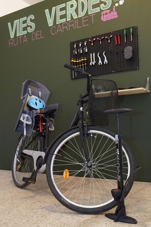 Una sedia a rotelle, una bicicletta e una bacheca con attrezzi su un muro verde.