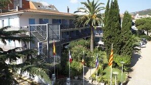 A hotel with a terrace, multiple flags, and a parking area. - Hotel Bell Repos (Castell-Platja d'Aro)