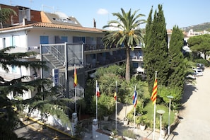 A hotel with a terrace, multiple flags, and a parking area. - Hotel Bell Repos (Castell-Platja d'Aro)