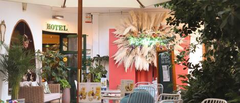 Hotellin sisustus, jossa on ruokailutila, rottinkihuonekaluja ja suuri koristeellinen kasvi.