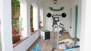 Un espacio exterior cubierto con equipo de ejercicio, incluyendo una bicicleta estática y una máquina de remo, y una pared con una frase motivacional.