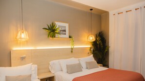 Habitación de hotel con una cama grande, mesitas de noche, cabecera con una imagen y dos lámparas colgantes.