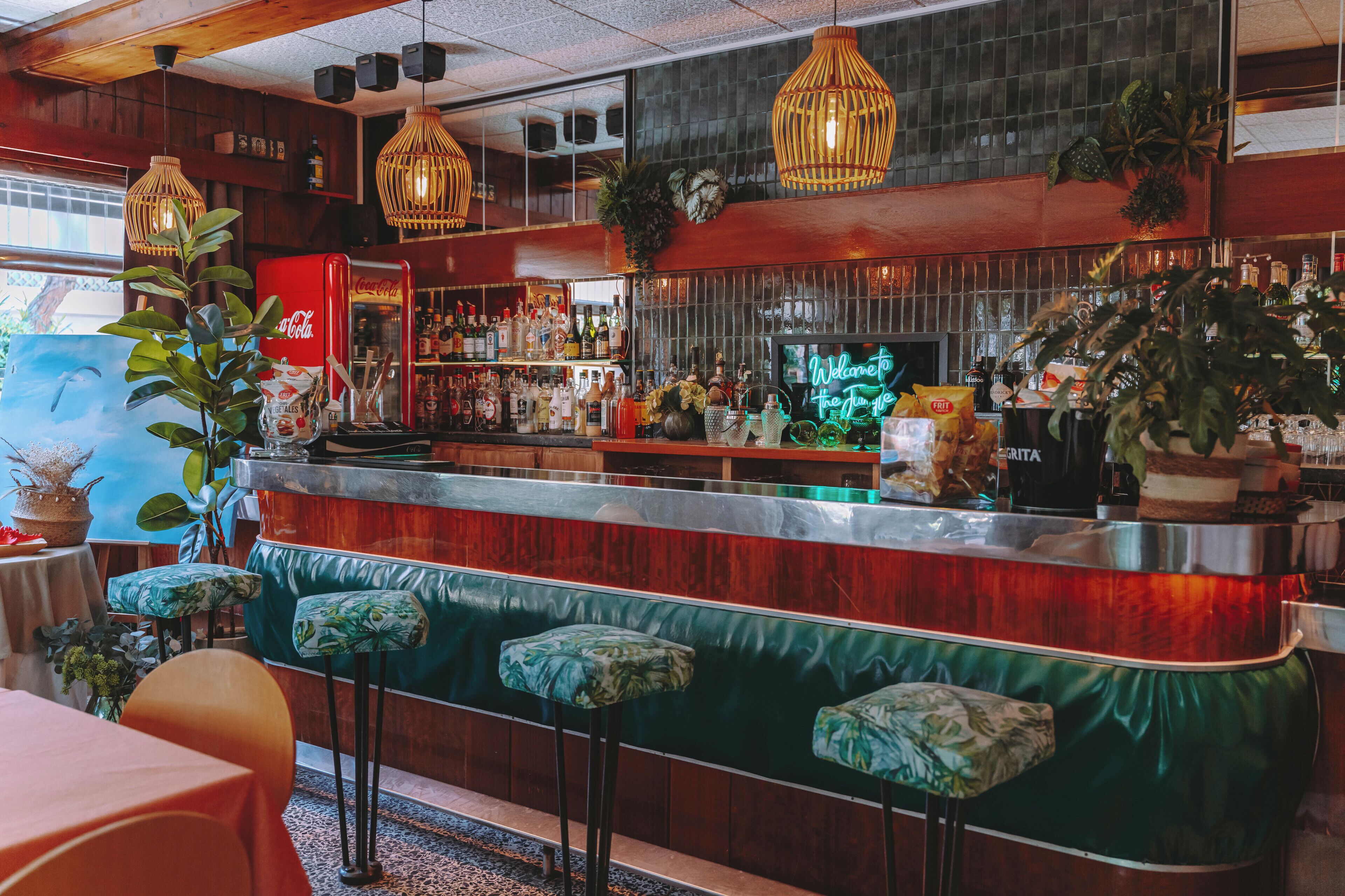 Een bar met een toonbank, krukken en diverse flessen.