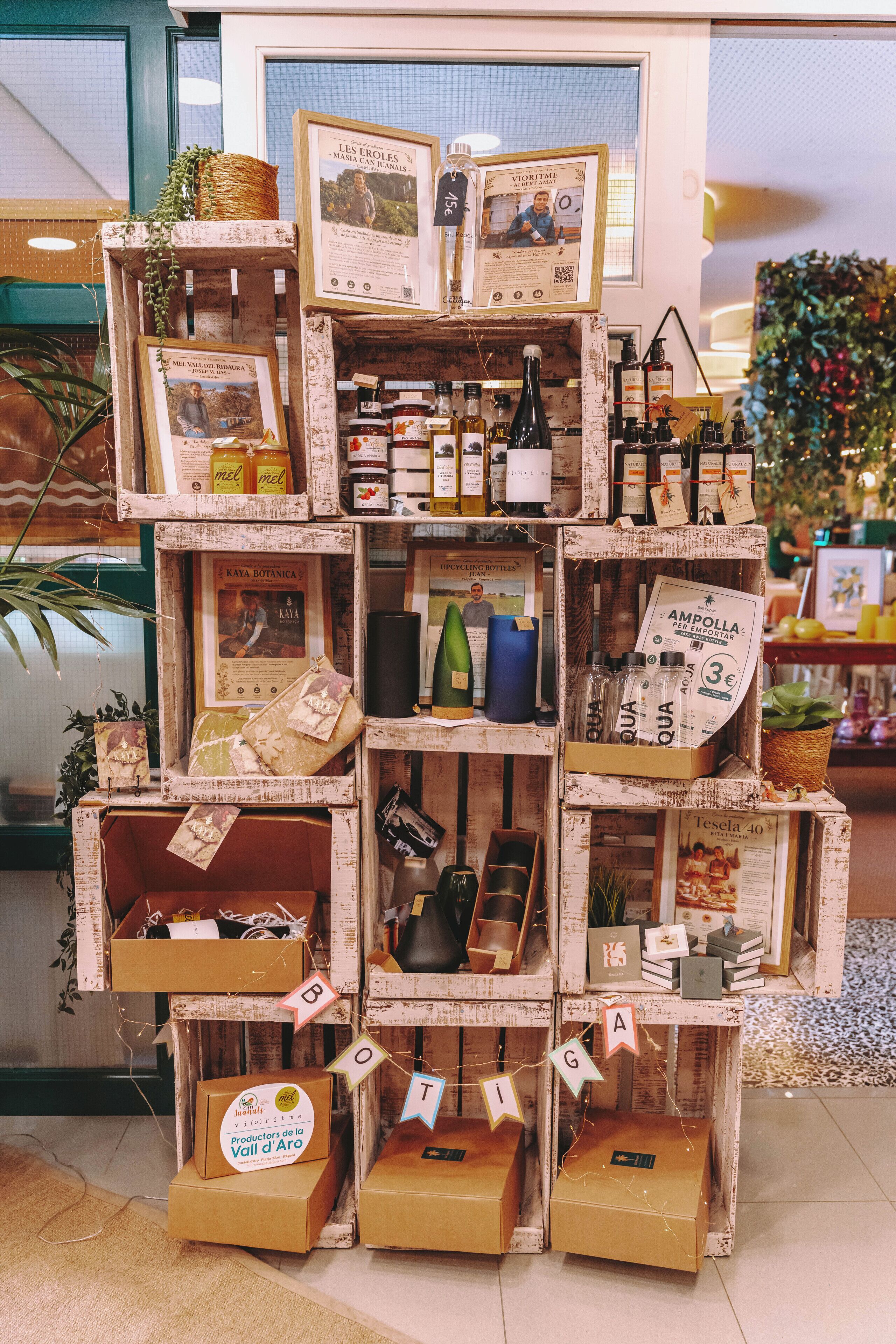 A display of various products including bottles, jars, and framed pictures, arranged on a wooden structure with labeled boxes at the base.