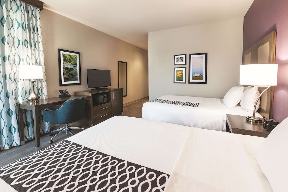 A hotel room with two beds, a desk with a computer, a TV, and a lamp.