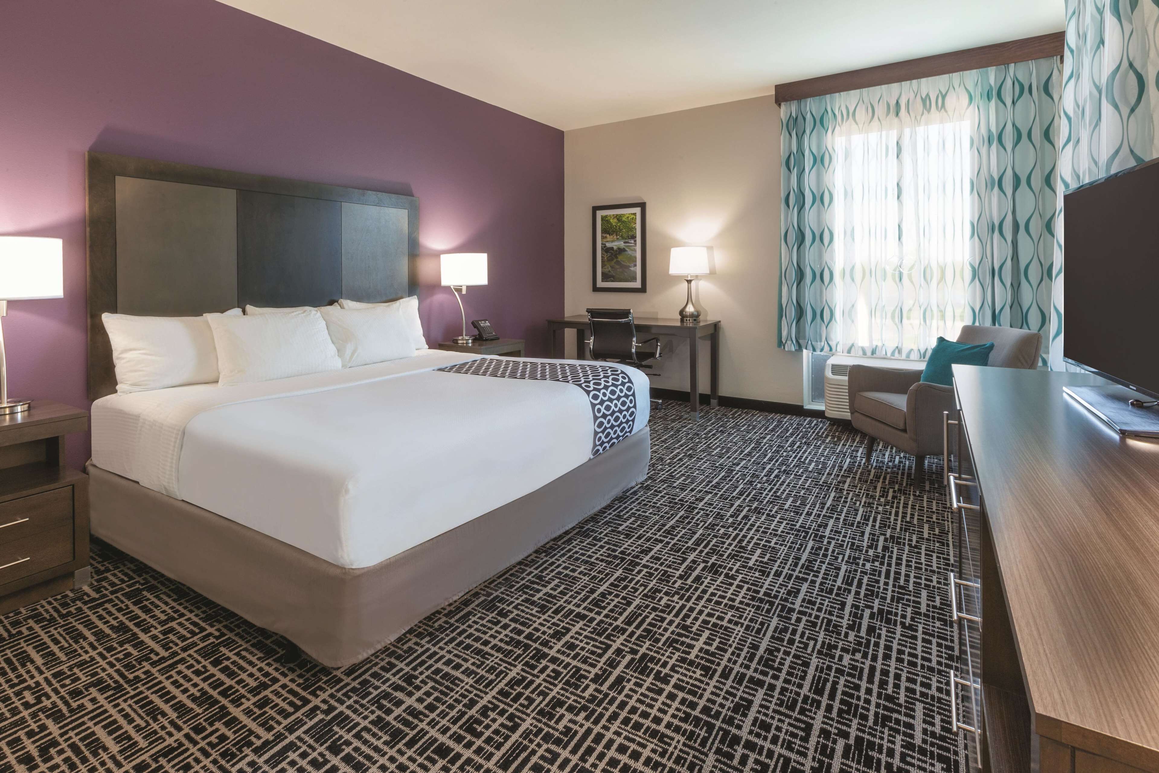 A hotel room with a large bed, a desk, a chair, and a TV.
