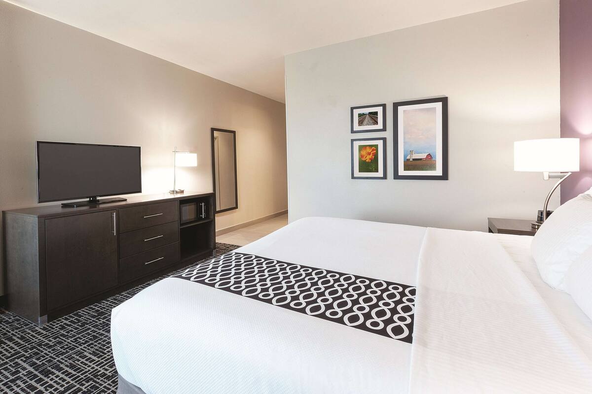A hotel room with a bed, a TV, a dresser, and framed pictures on the wall.