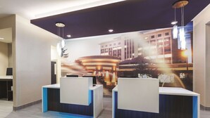 A reception area with two reception desks, a modern ceiling design, and a large wall mural. - La Quinta Inn & Suites by Wyndham Terre Haute (Terre Haute)