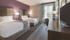 A hotel room with two beds, a desk, a chair, a TV, and a window with curtains. - La Quinta Inn & Suites by Wyndham Terre Haute (Terre Haute)