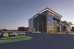 A La Quinta Inn & Suites building with a modern design, featuring a large signboard, a covered entrance, and a parking area.