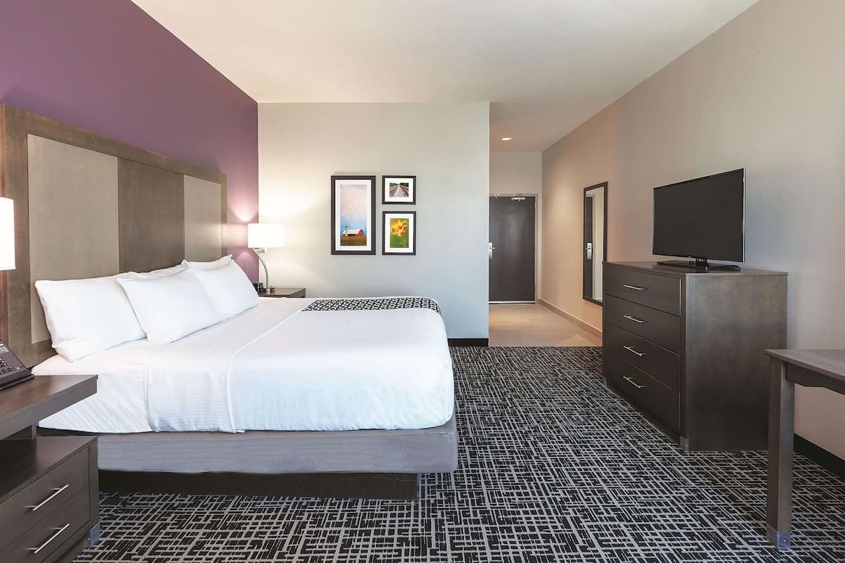 A hotel room with a bed, a dresser, a television, and framed pictures on the wall.