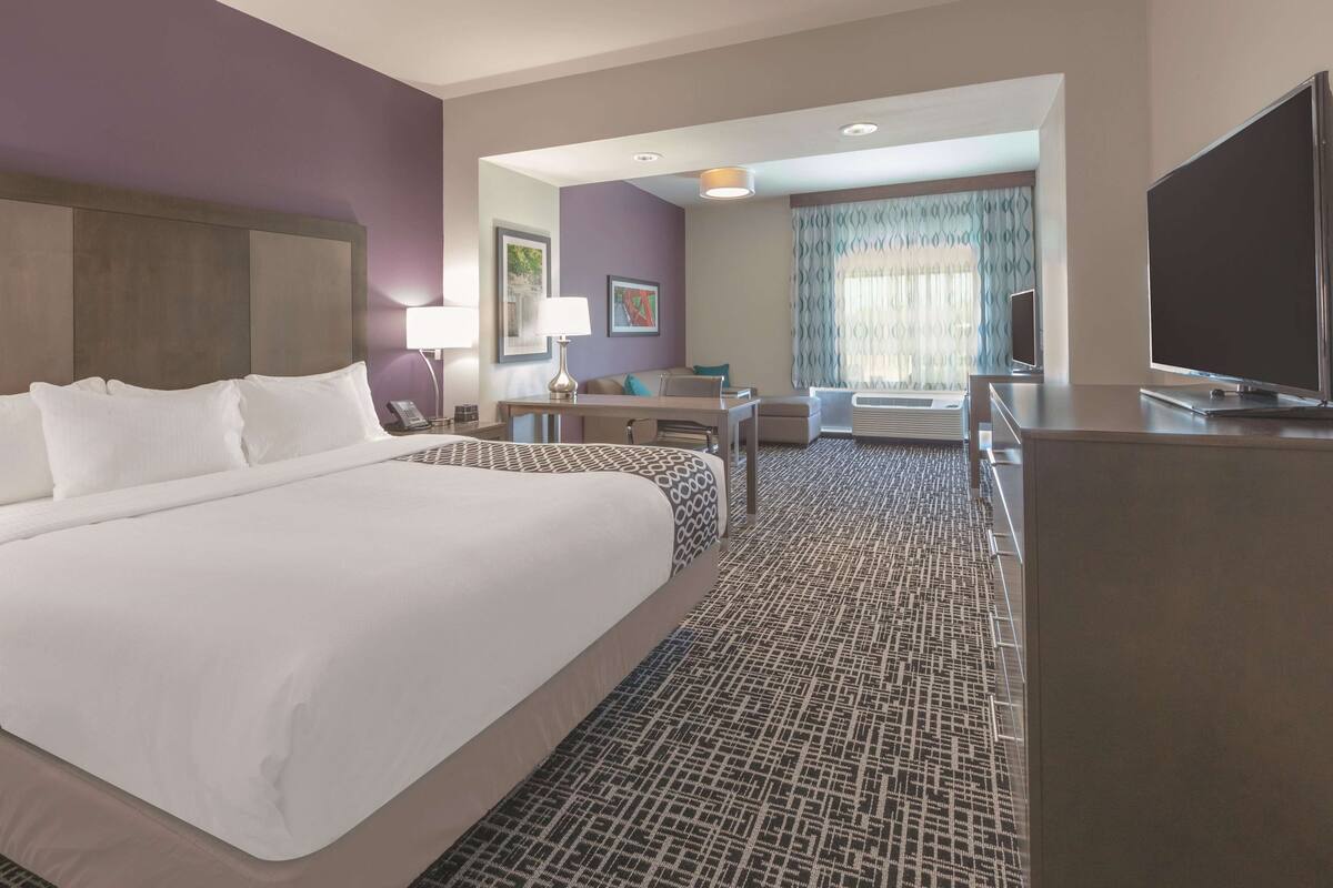 A hotel room with a large bed, a desk, a chair, a TV, and a window with curtains.