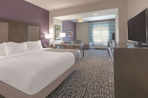 A hotel room with a large bed, a desk, a chair, a TV, and a window with curtains.