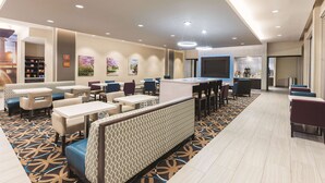 A hotel lobby with seating areas, a reception desk, and a large TV screen. - La Quinta Inn & Suites by Wyndham Terre Haute (Terre Haute)