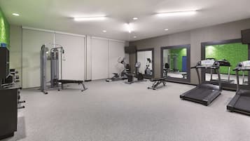 Un gimnasio moderno con máquinas de cardio, equipo de entrenamiento de fuerza y un espejo grande.