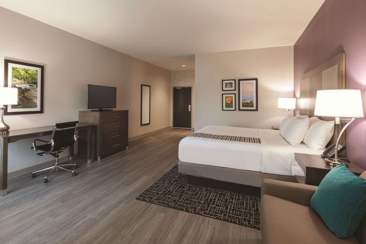 A hotel room with a bed, desk, chair, dresser, and a TV.