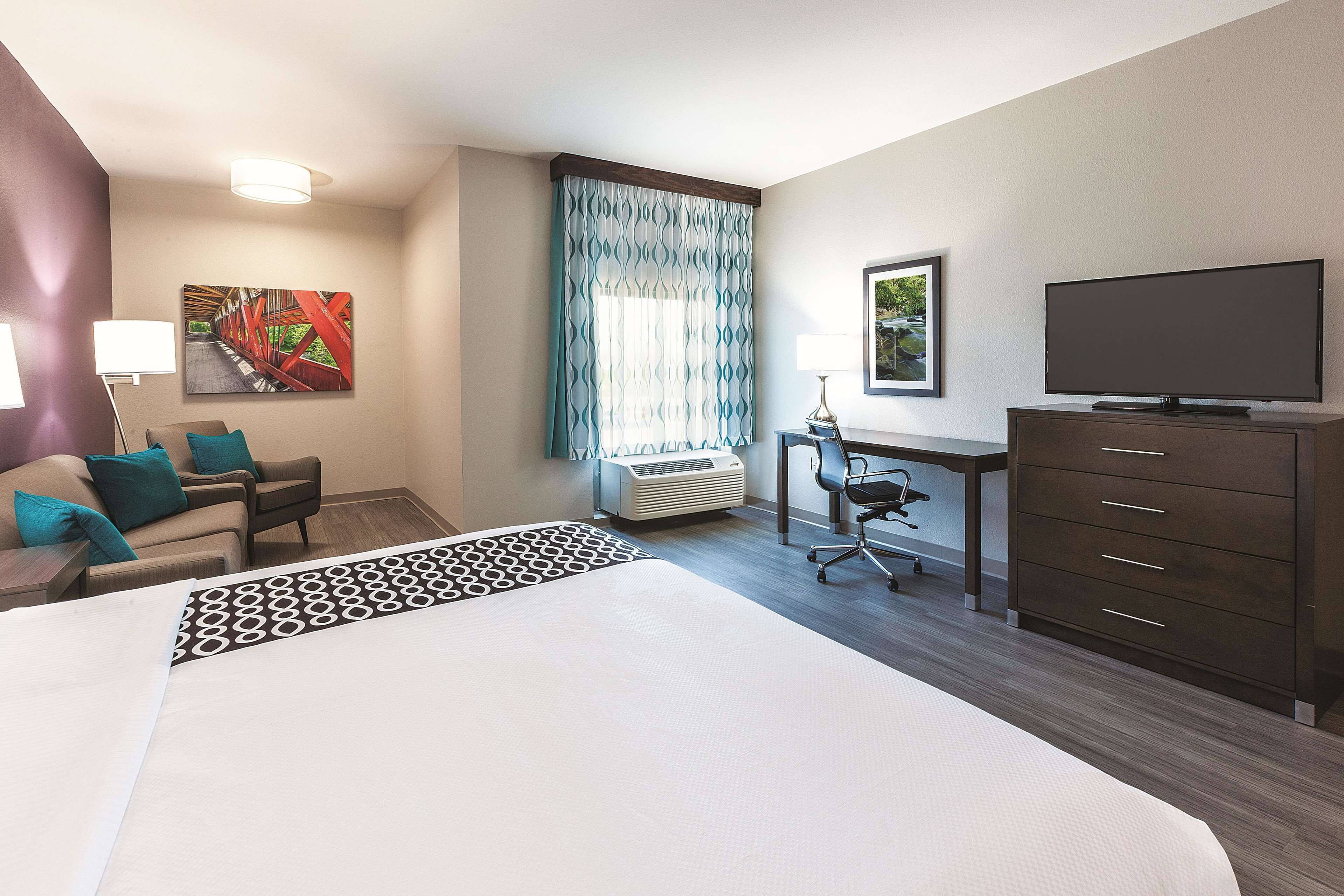 A hotel room with a large bed, a desk, a chair, a television, and a window with curtains.