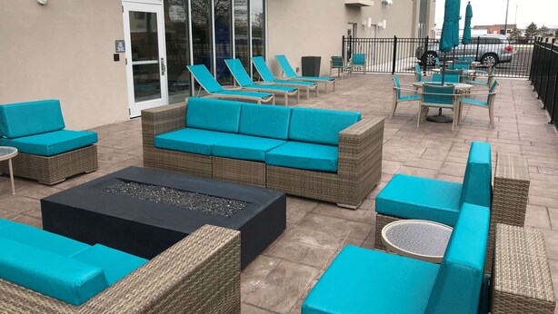 An outdoor seating area with wicker furniture and teal cushions, a fire pit, and umbrellas. - La Quinta Inn & Suites by Wyndham Terre Haute (Terre Haute)