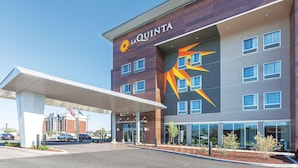 A La Quinta hotel with a modern design, featuring a large logo on the facade, a covered entrance, and a parking area. - La Quinta Inn & Suites by Wyndham Terre Haute (Terre Haute)