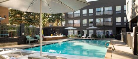 Ein Swimmingpool mit Liegestühlen und Sonnenschirmen, umgeben von einem Gebäude mit mehreren Fenstern und Balkonen.