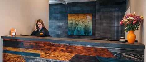 En reception med en træbordplade og et mønstret design, en receptionist og et billede på væggen.