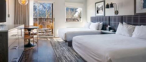 A hotel room with two beds, a desk, a chair, a TV, and a window with a view of trees and mountains.