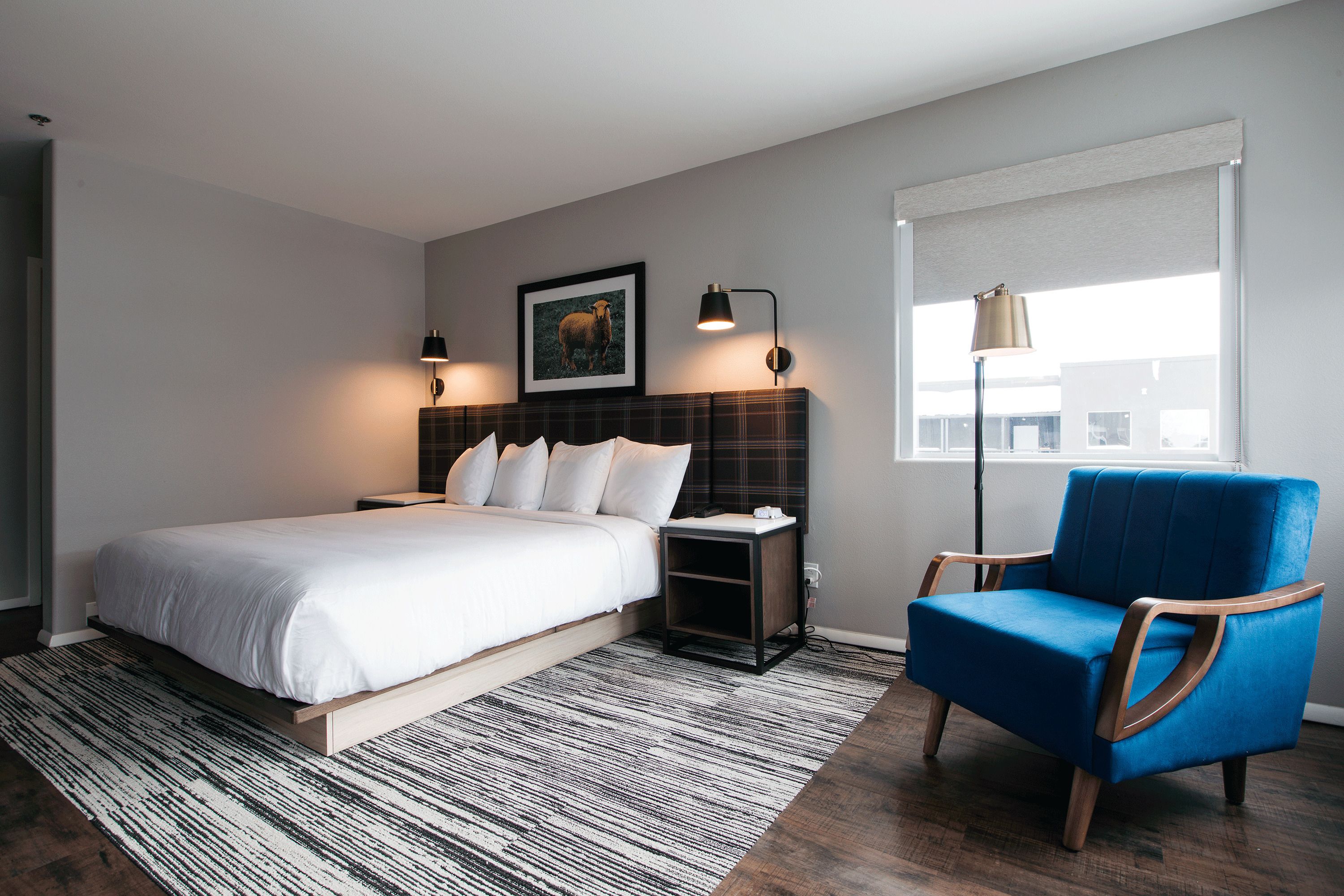 A bedroom with a bed, bedside tables, a chair, a window, and a picture on the wall.