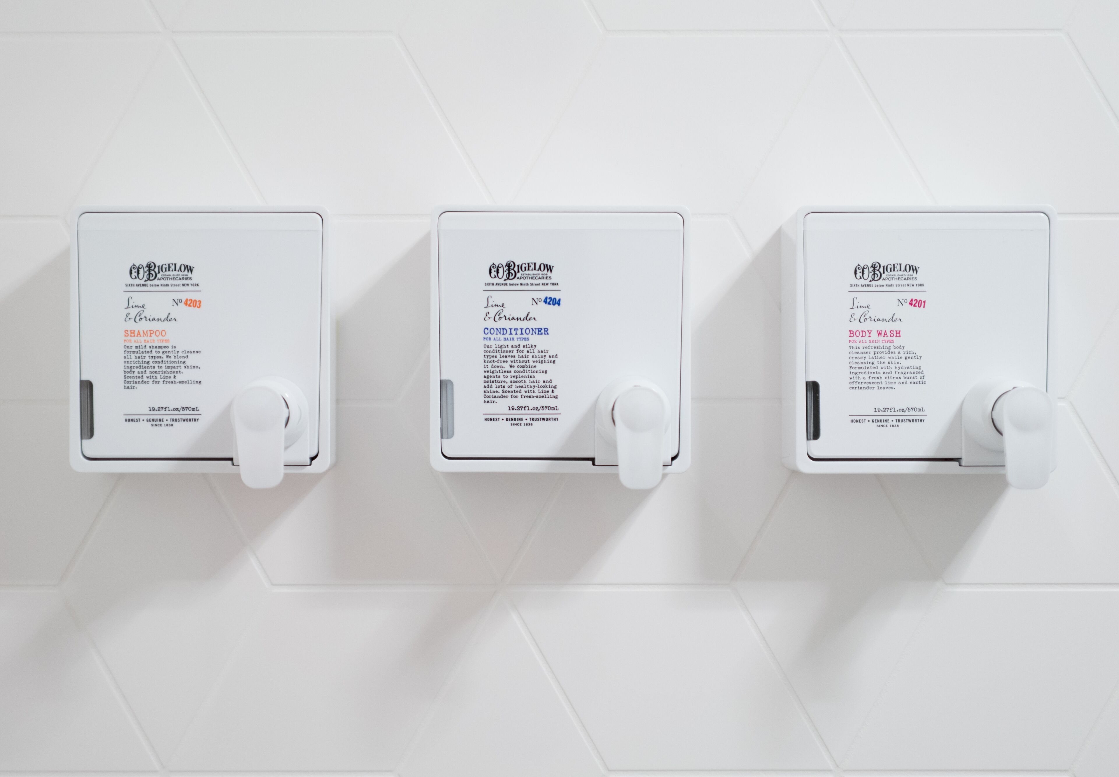Drei an der Wand befestigte Spender für Shampoo, Conditioner und Duschgel.