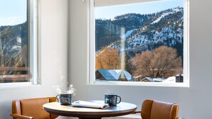 A room with a view of a snowy mountain, a table with two mugs, and a chair. - Hotel Ketchum (Ketchum)