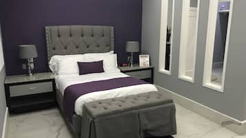 Un dormitorio moderno con un cabecero capitonado, un banco gris y una manta morada.