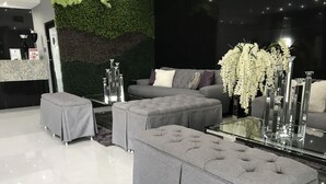 A modern living room with grey upholstered sofas, a glass coffee table, and a green wall with foliage.