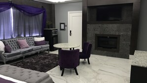 A modern living room with a grey sofa, purple cushions, a round table, and a fireplace.