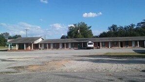 A motel with a row of rooms, a covered parking area, and a small building with a sign. - Royal Inn (Honea Path)