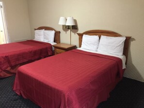 A hotel room with two beds, each with a red bedspread and white pillows. There is a nightstand with a lamp between the beds. - Royal Inn (Honea Path)