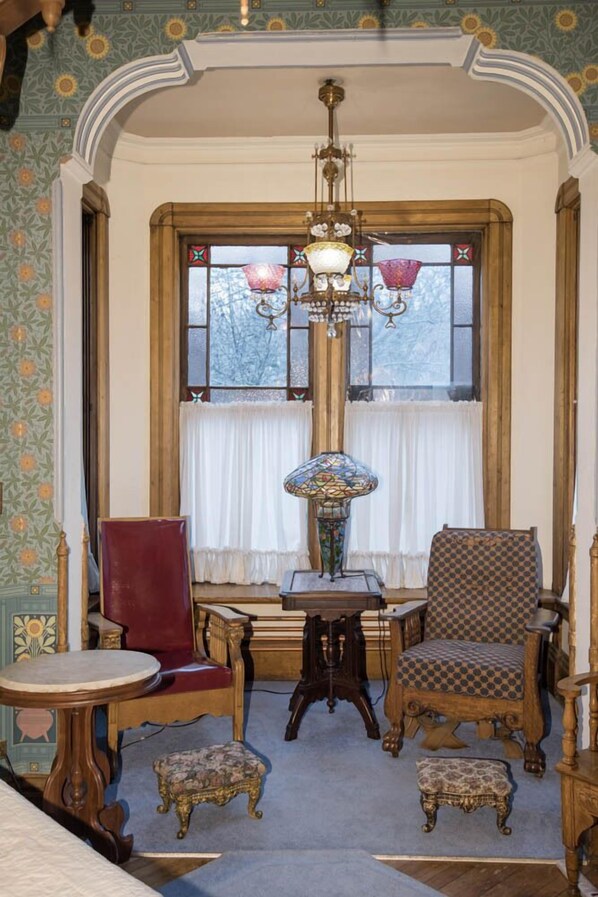 Une pièce comprenant une chaise en bois, une chaise rouge, une table et une lampe.