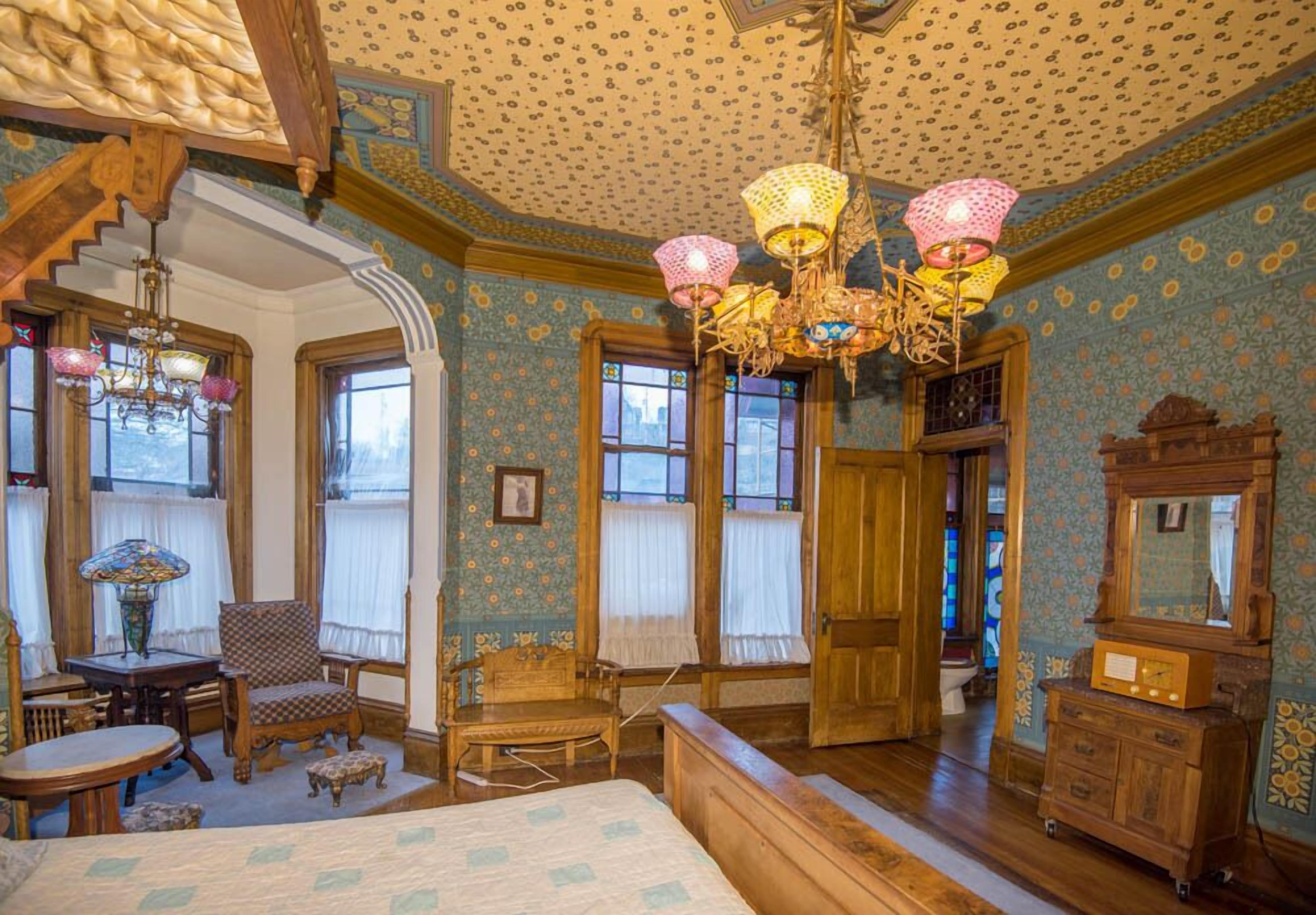 A room with a bed, wooden furniture, a chandelier, and patterned wallpaper.