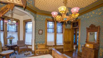 A room with a bed, wooden furniture, a chandelier, and patterned wallpaper.