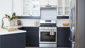 Een moderne keuken met donkere kastjes, witte aanrechtbladen, een roestvrijstalen koelkast en een ingebouwde oven.