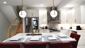 Een moderne keuken met witte kasten, een roestvrijstalen koelkast, een inbouwoven en een eethoek met rode stoelen en een witte tafel gedekt voor vier personen.