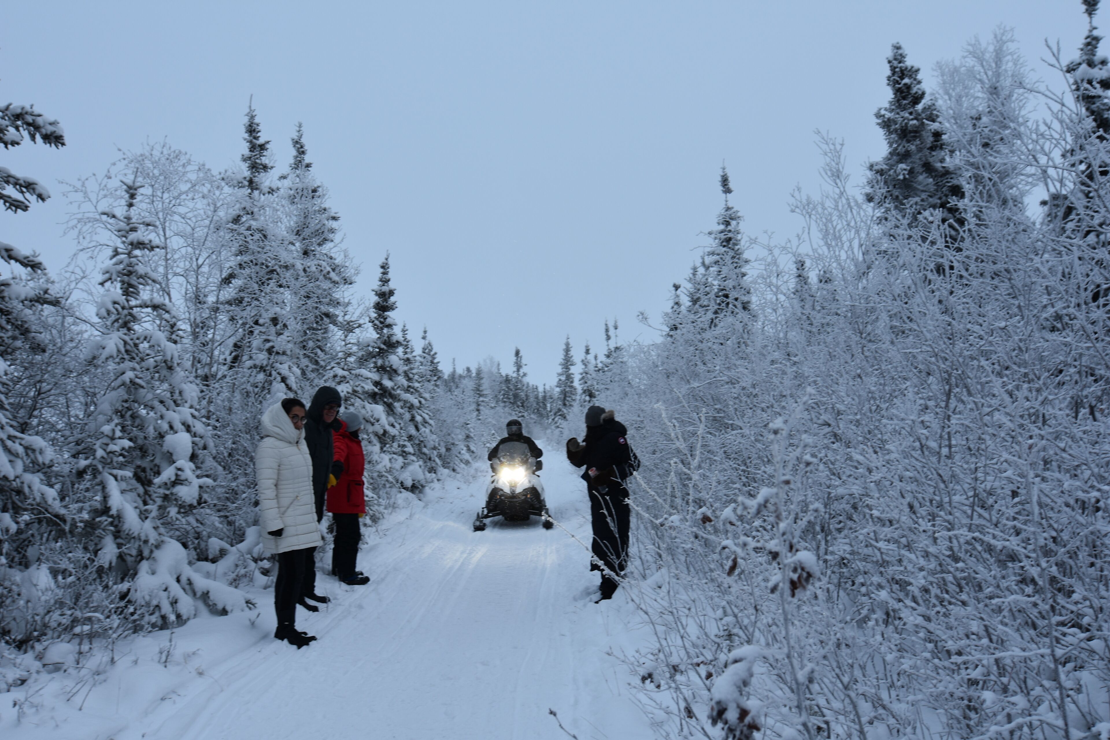 A snow-covered path with people and a snowmobile.