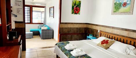 A hotel room with a bed, a desk, a chair, a small table, and a ceiling fan.