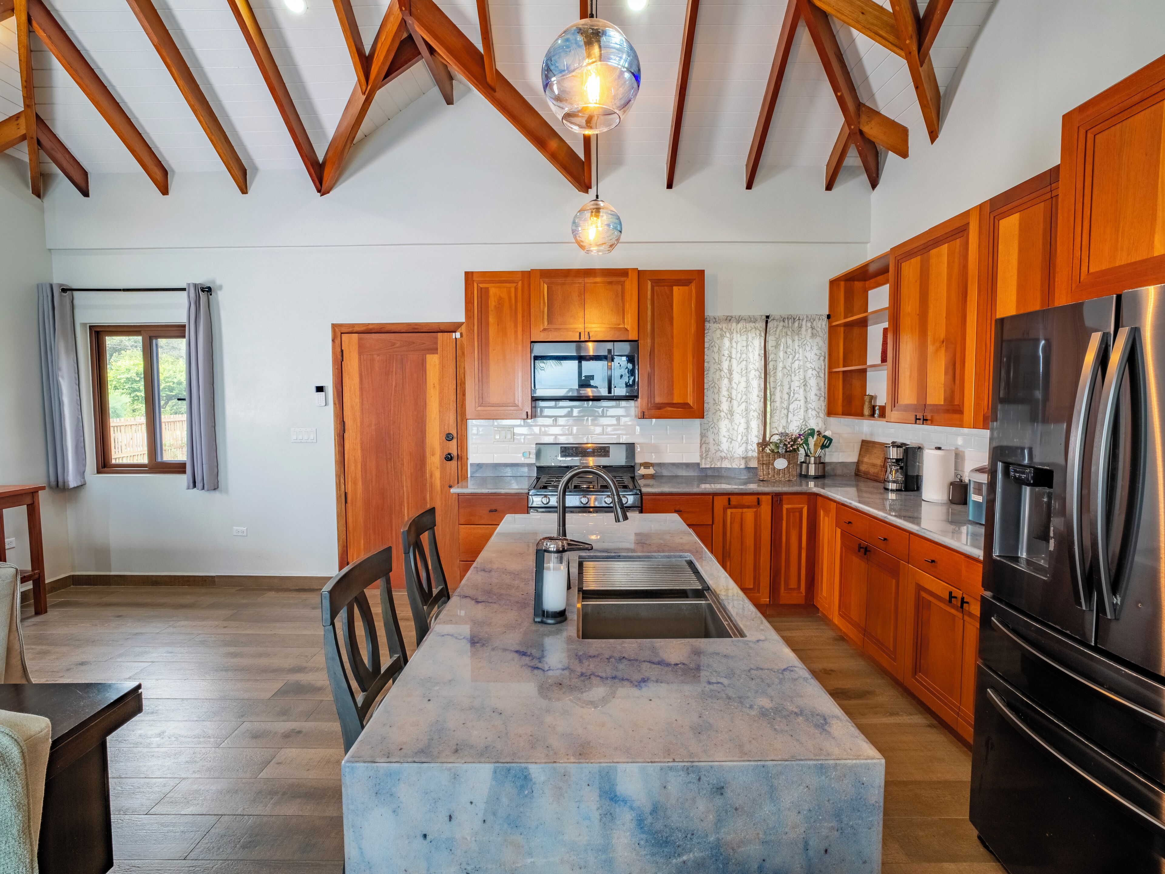 Une cuisine moderne avec des meubles en bois, un îlot en marbre, des appareils électroménagers en acier inoxydable et un plafond voûté.