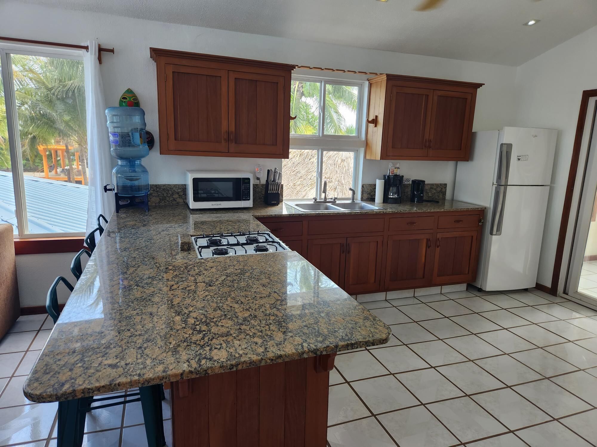 Una cocina con encimeras de granito, gabinetes de madera, estufa a gas, microondas, refrigerador y dispensador de agua.