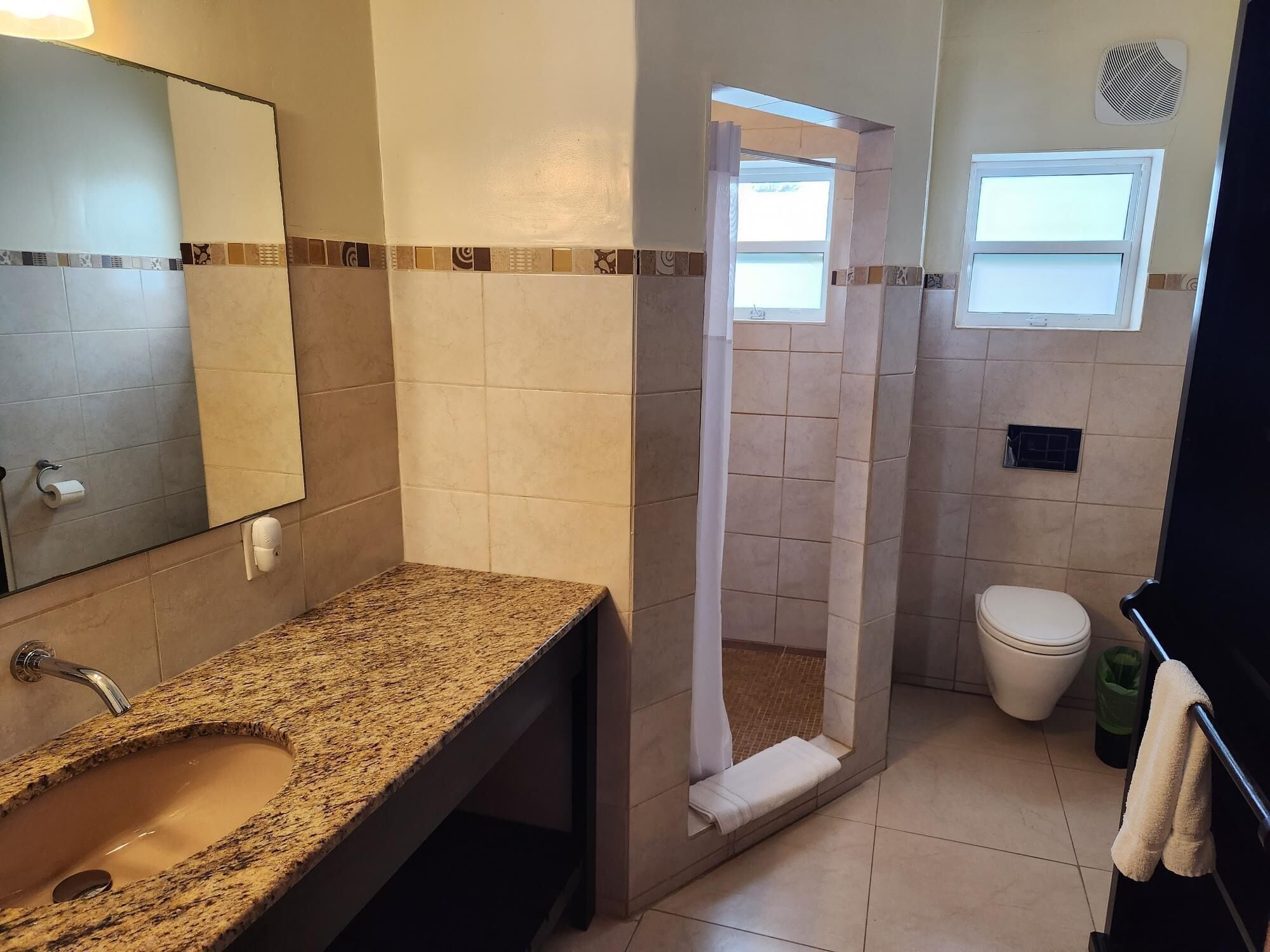 A bathroom with a granite sink, a mirror, a shower enclosure, a toilet, and a window.