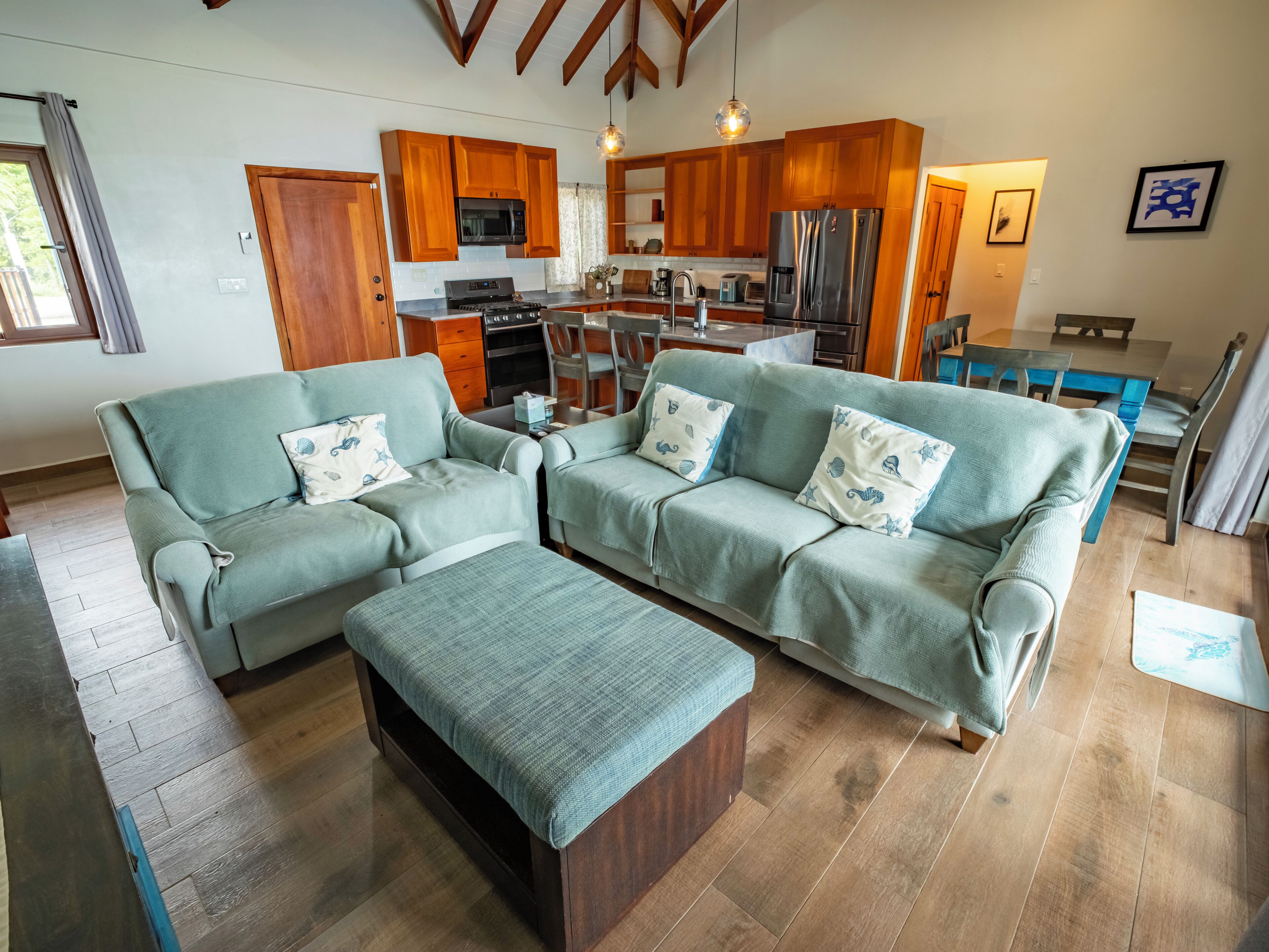 A spacious living room with a sofa set, a dining table, and a kitchen area with wooden cabinets and appliances.