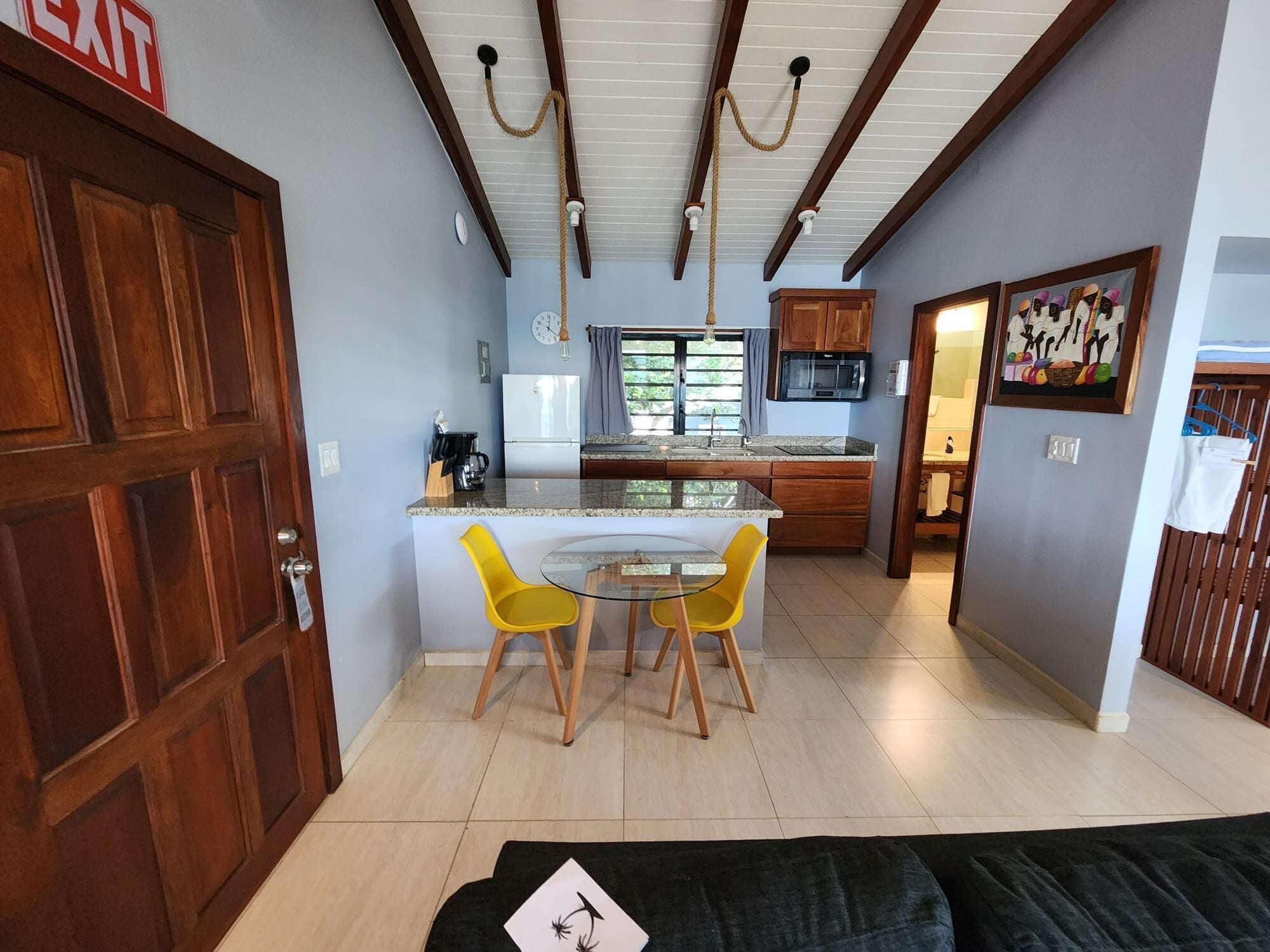 Cocina compacta con comedor, puerta de madera y una pequeña mesa con sillas amarillas.