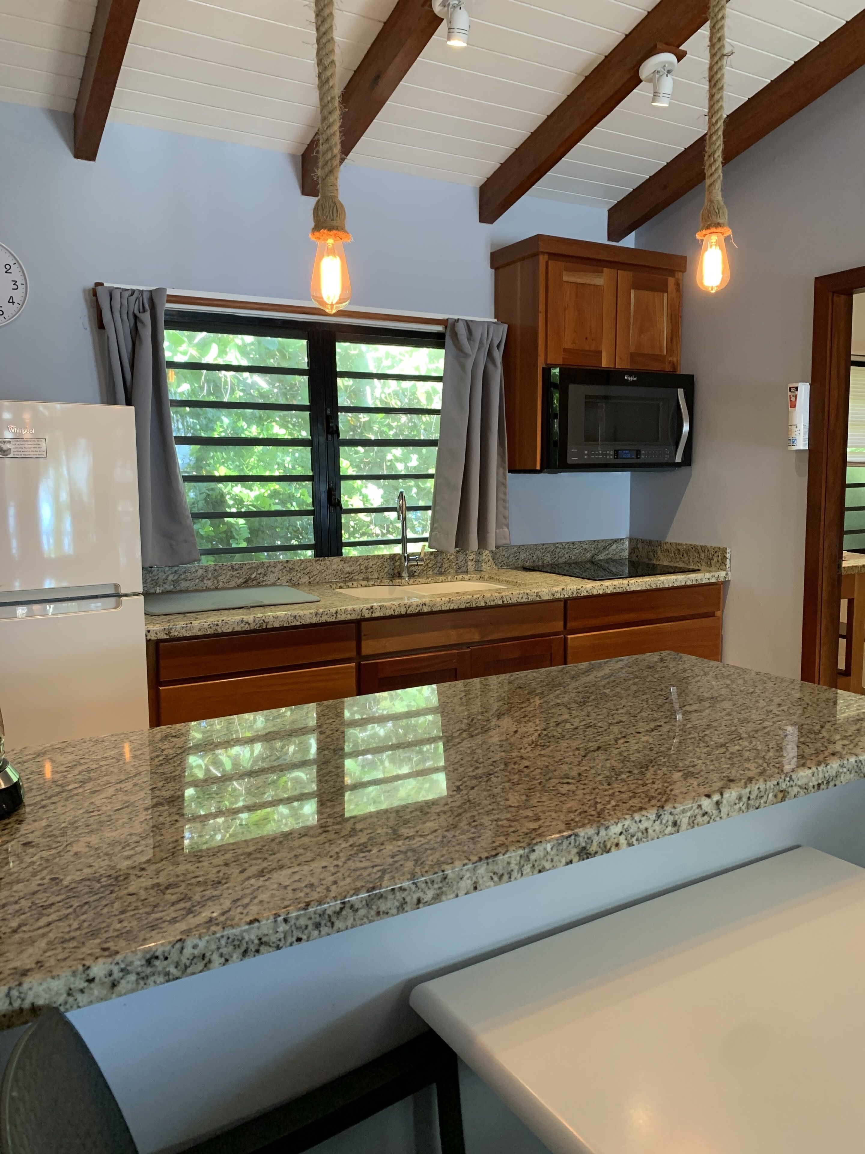 A kitchen with granite countertops, wooden cabinets, a built-in microwave, and pendant lights.