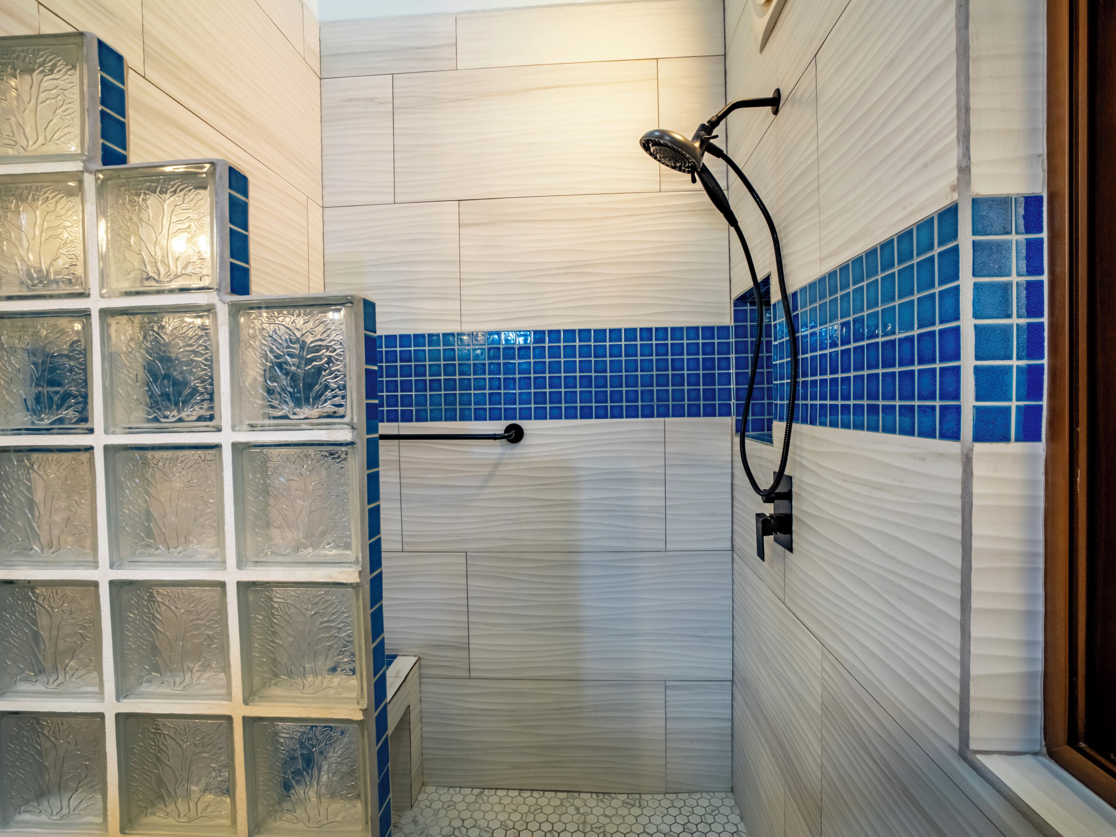 A shower with a handheld showerhead, tiled walls, and a glass block wall.