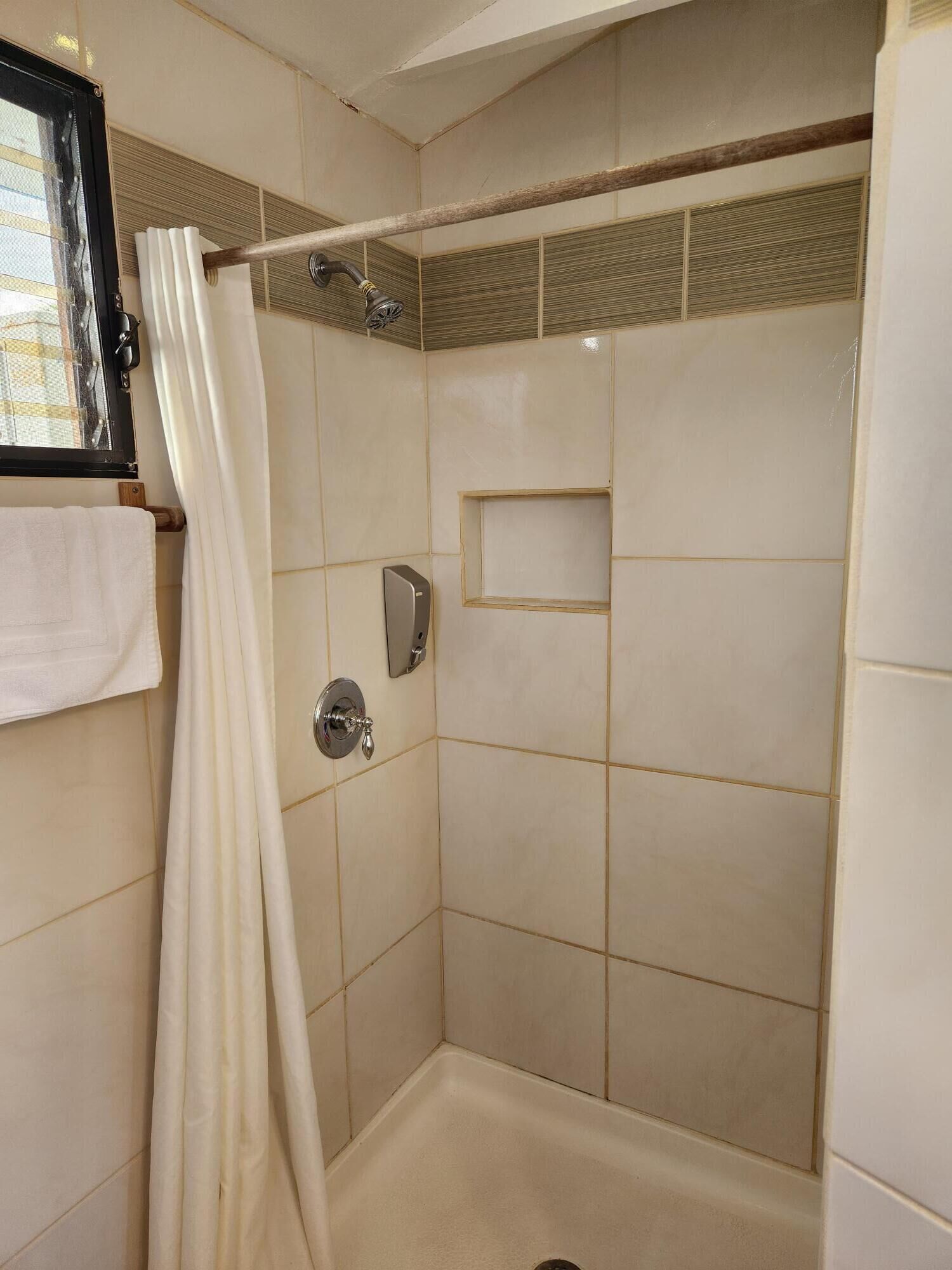 Una ducha con azulejos color beige, una puerta de cristal, un perchero para toallas y un dispensador de jabón.